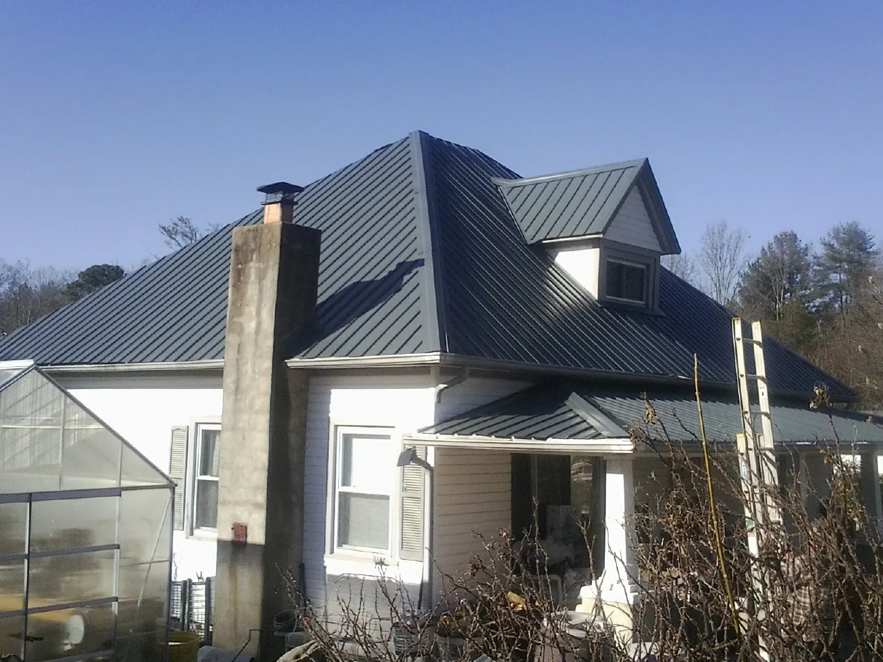 Dark blue standing seam metal roof on a white farmhouse with dormer — Slate & Tile Roof Repair by Roofing Brothers in Fruita