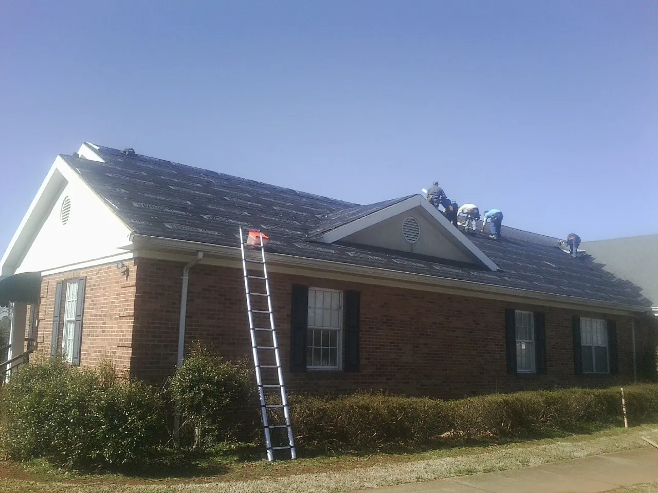 Crew tearing shingles off a brick ranch roof with a ladder set — Emergency Roof Repair work by our crew in Fruita