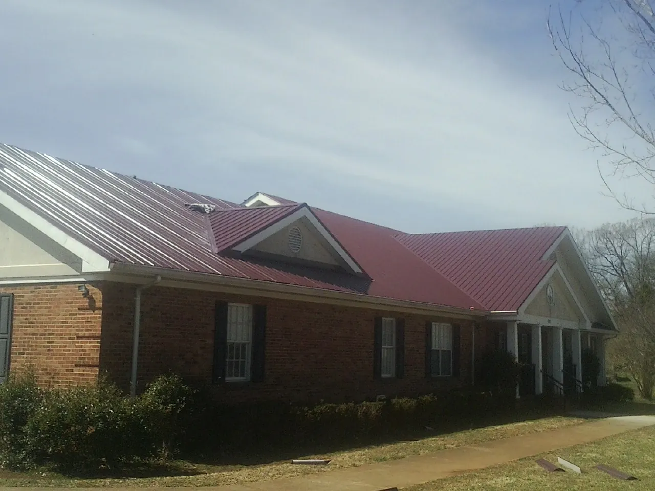 Red metal roof with gabled entries on a long brick building, from a Hail Damage Roof Repair job in Fruita