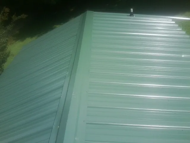 New green metal panels meeting at the ridge of a roof — Flat Roof Repair work by our crew in Fruita