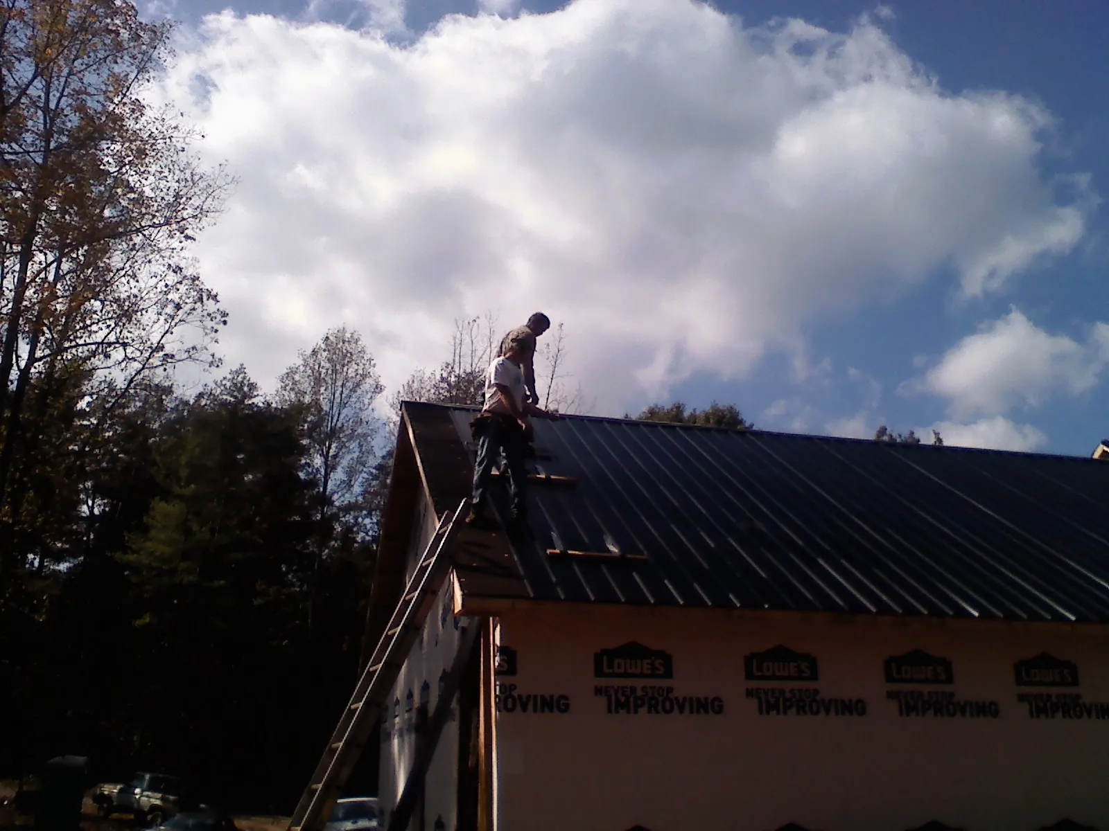 Roofer fastening dark metal panels high against a cloudy sky, from a Roof Inspection job in Fruita