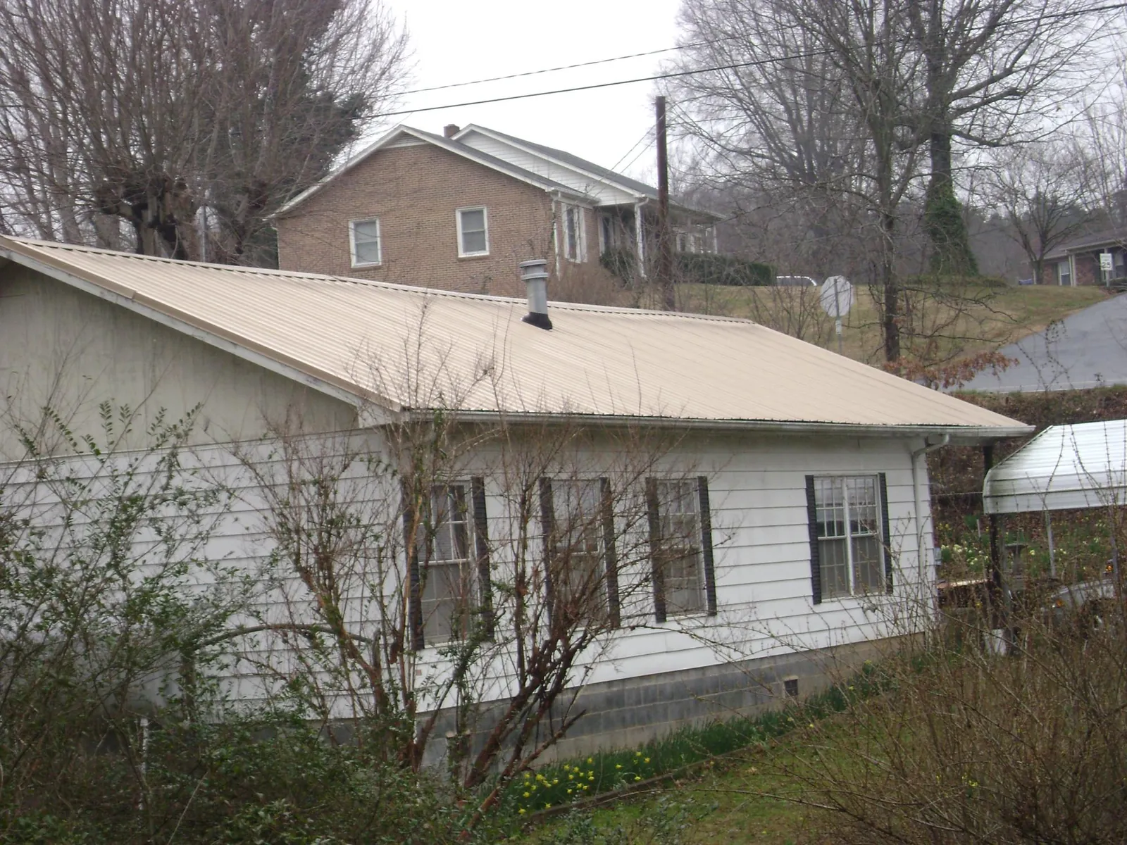 Tan metal roof on a white sided house set into a hillside — Commercial Roofing by Roofing Brothers in Fruita